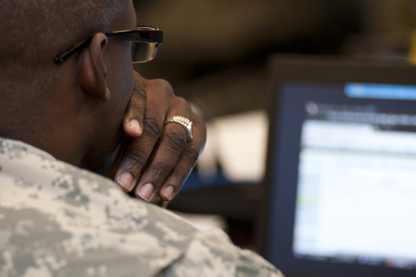 Photo over the shoulder of a soldier looking at a computer screen